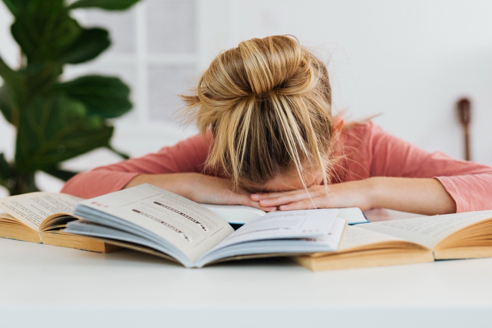A tired student resting her head on a stack of open books
